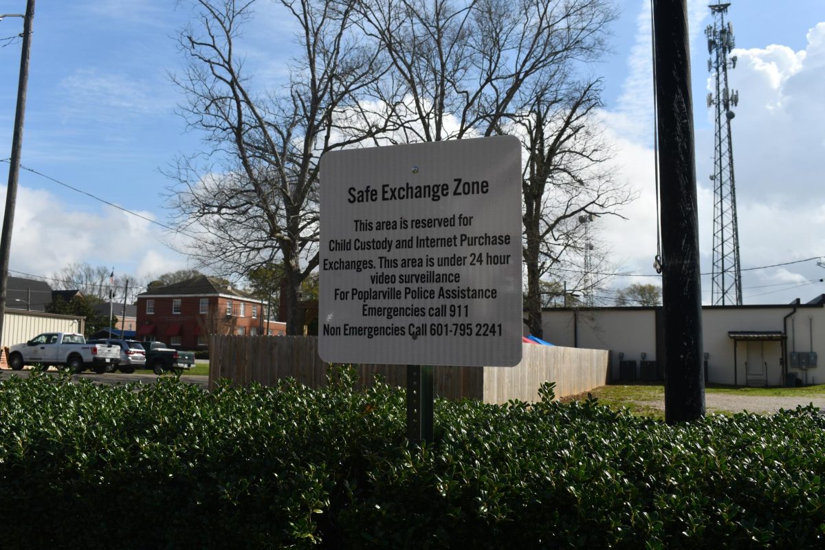 A sign in front of bushes reads “Safe Exchange Zone” with information about the zone.