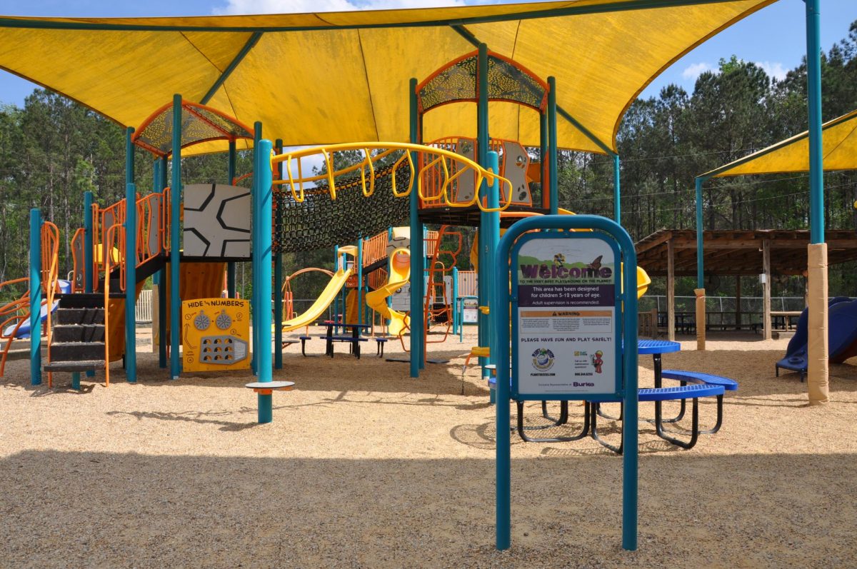 A bright yellow and teal playground with stairs, bars, shade structures and slides.