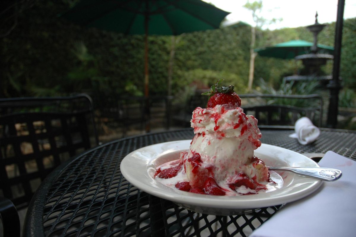 Strawberry shortcake dessert topped with whipped cream on a white plate in a restaurant dining area.
