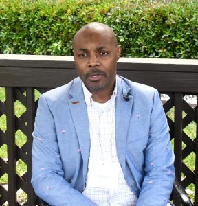 Darien Spann sits outdoors wearing a light blue blazer during an interview.