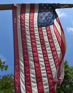 A red, white and blue U.S. flag hangs from a pole against a blue sky.