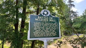 A green and gray historical marker with yellow text describes the Battle of McLeod’s Mill.