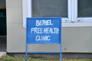 A blue hand-painted sign reading “Bethel Free Health Clinic.”