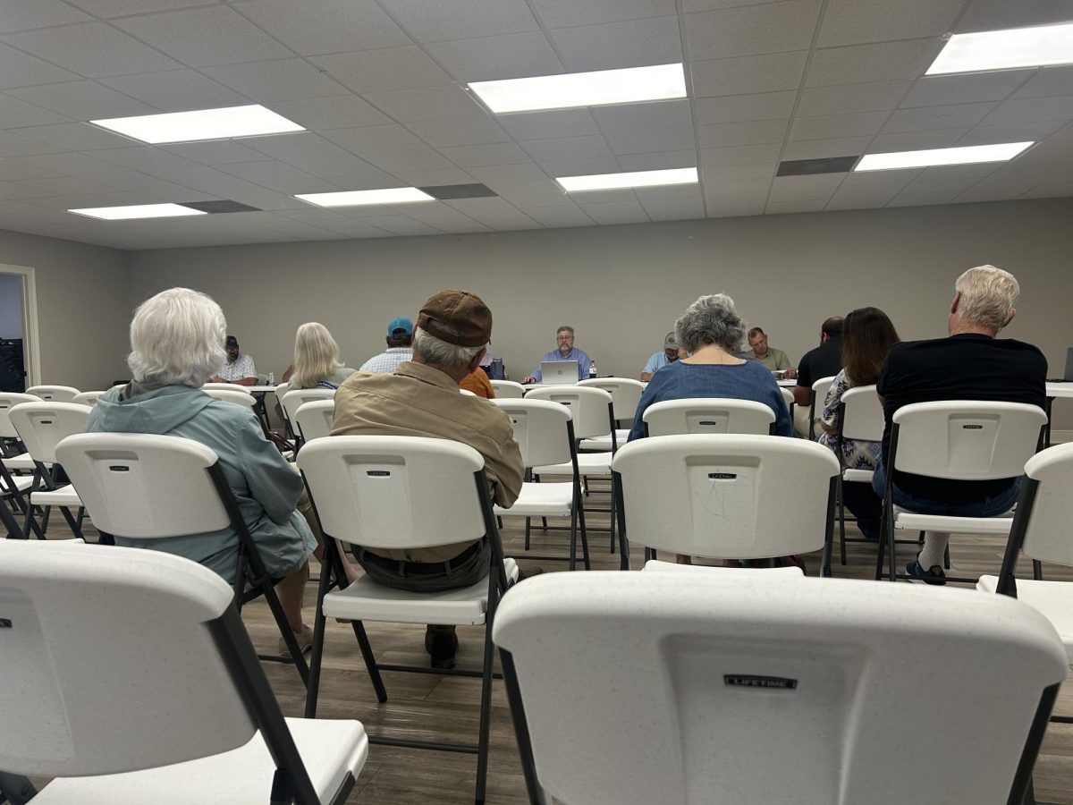 Thirteen people sit in white folding chairs in a room during a board meeting with water association officials.