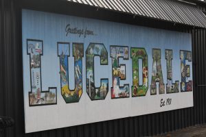 A large mural on a building reads “Greetings from Lucedale” and features illustrated scenes inside the letters.