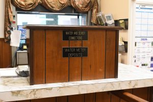 A wooden service counter inside Lucedale City Hall displays signs for water and sewer connections and water meter deposits.