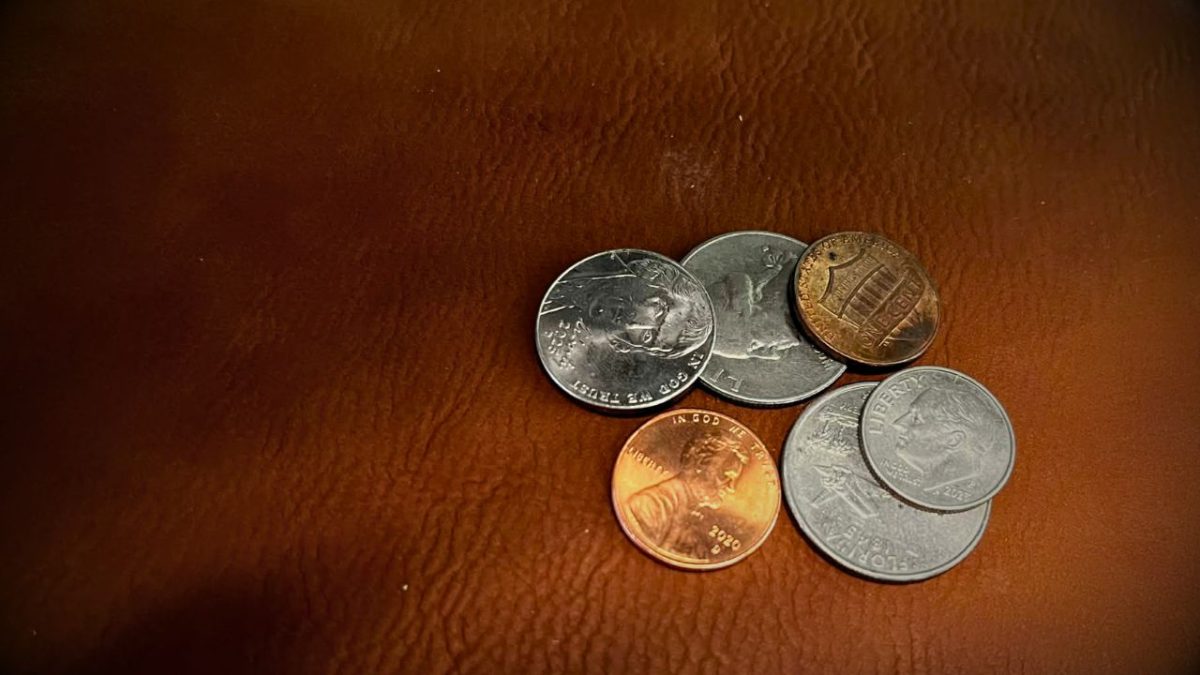 A small pile of U.S. coins, including two pennies, sit on a wooden table.