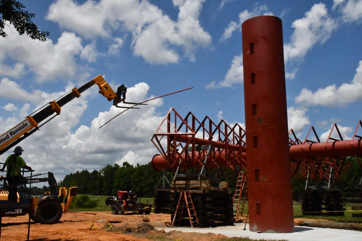 A construction worker controls a crane, delivering materials to the horizontal crossbeam of the cross.