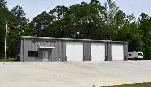 A fire station with three garage bays, an American flag and a white vehicle parked nearby.