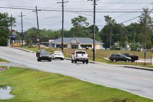 Vehicles drive along a wet roadway near businesses and utility poles.