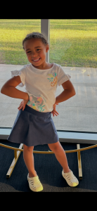 Ava Maie smiles while standing in front of a large window.