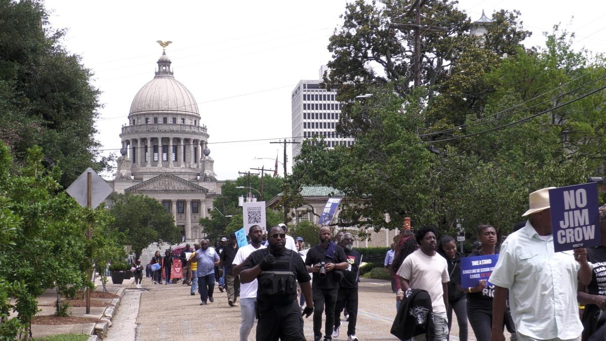 A large crowd of people holding signs walks down a street with a government building in the background.