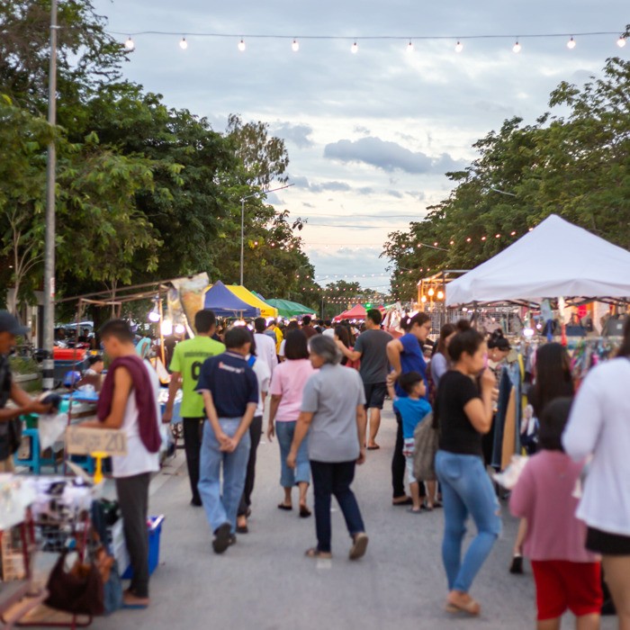 A well-lit paved road where residents and visitors explore booths selling various crafts.