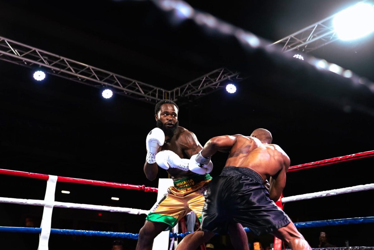 Boxer in green and yellow shorts prepares to punch boxer in black shorts during boxing match.