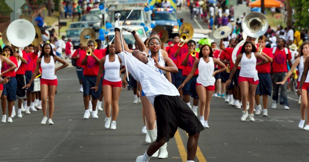 A parade performer leans backward while twirling a baton in front of marching band members and dancers during a Juneteenth parade in Hattiesburg.