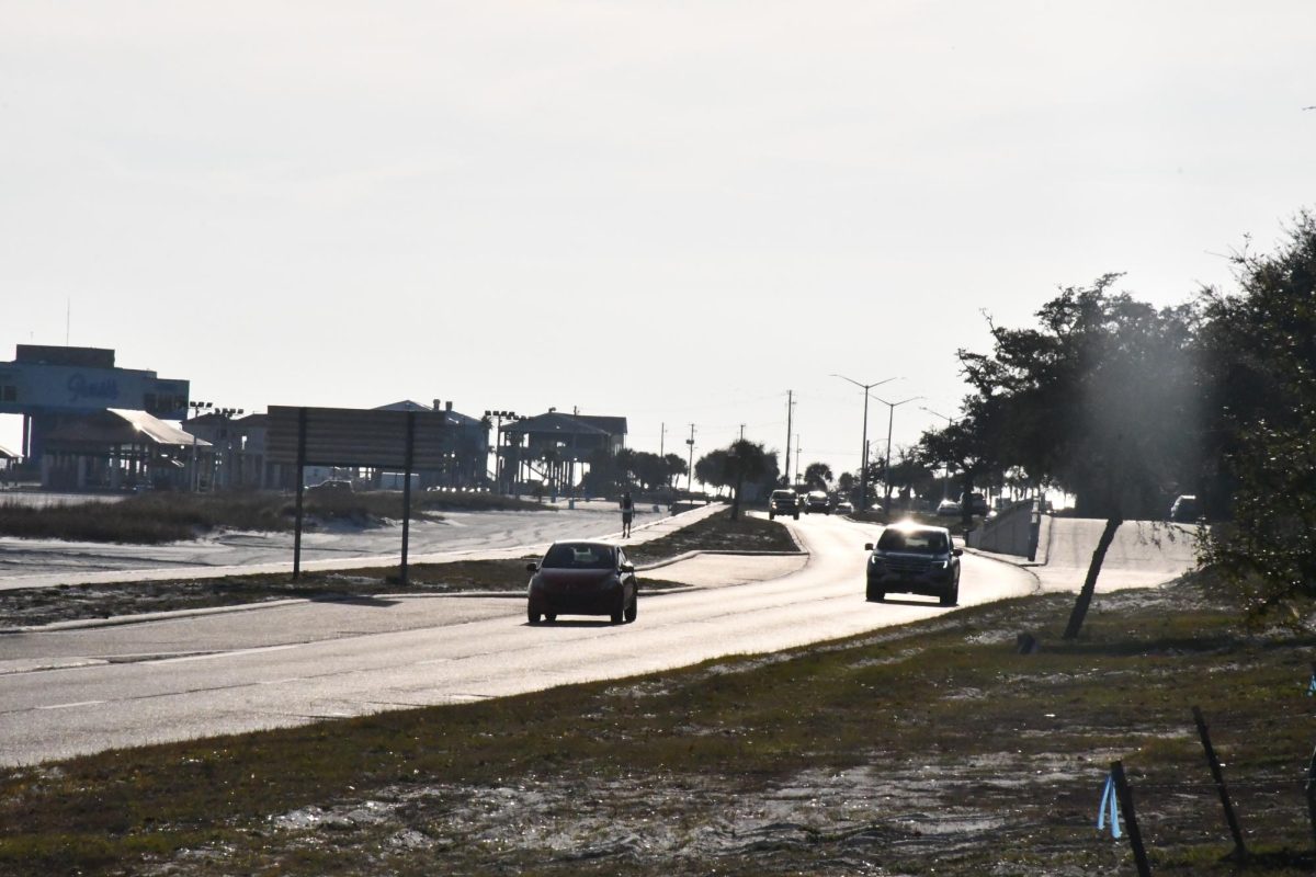 Cars drive on a sunlit road near beachside buildings in Mississippi.