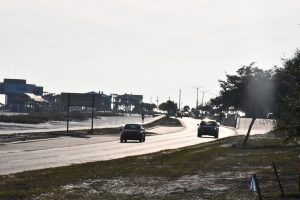 Cars drive on a sunlit road near beachside buildings in Mississippi.