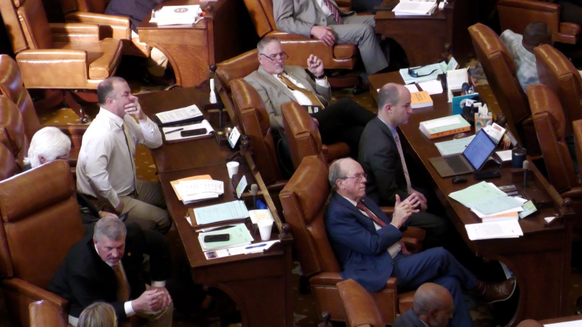 Members of the Mississippi House sit at desks on the chamber floor during a legislative session. Papers, laptops and leather-backed chairs are visible throughout the room.