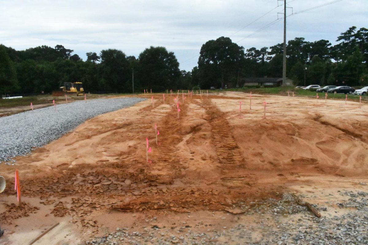 A cleared construction site with graded dirt, survey stakes marked with pink flags, a gravel base and heavy equipment shows early site work for a future 7 Brew drive-thru coffee stand in Petal, Mississippi.