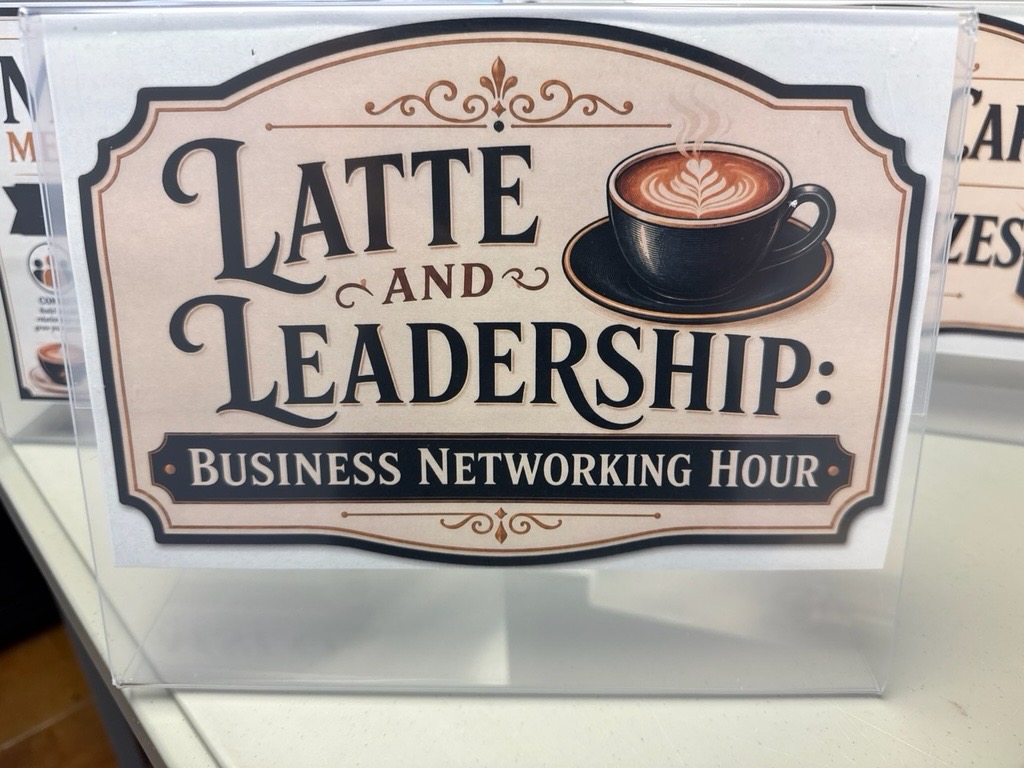 A small display sign advertises the “Latte and Leadership: Business Networking Hour” event. Featuring a steaming navy coffee cup graphic and a large “Latte and Leadership Business Networking Hour” text in the text color of navy presented on a white background.