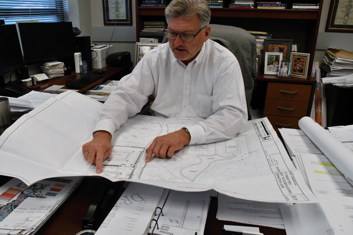 Jerry Creel points to a large site plan spread across a desk in an office.