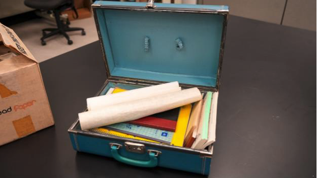 An open blue suitcase filled with documents, notebooks and rolled papers sits on a dark table as part of the 1960s-era Ku Klux Klan materials held by the Mississippi Department of Archives and History.