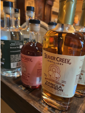 Several bottles of Beaver Creek Distillery spirits sit on a wooden display shelf.