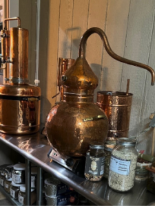A small copper still and glass jars sit on a stainless-steel worktable.