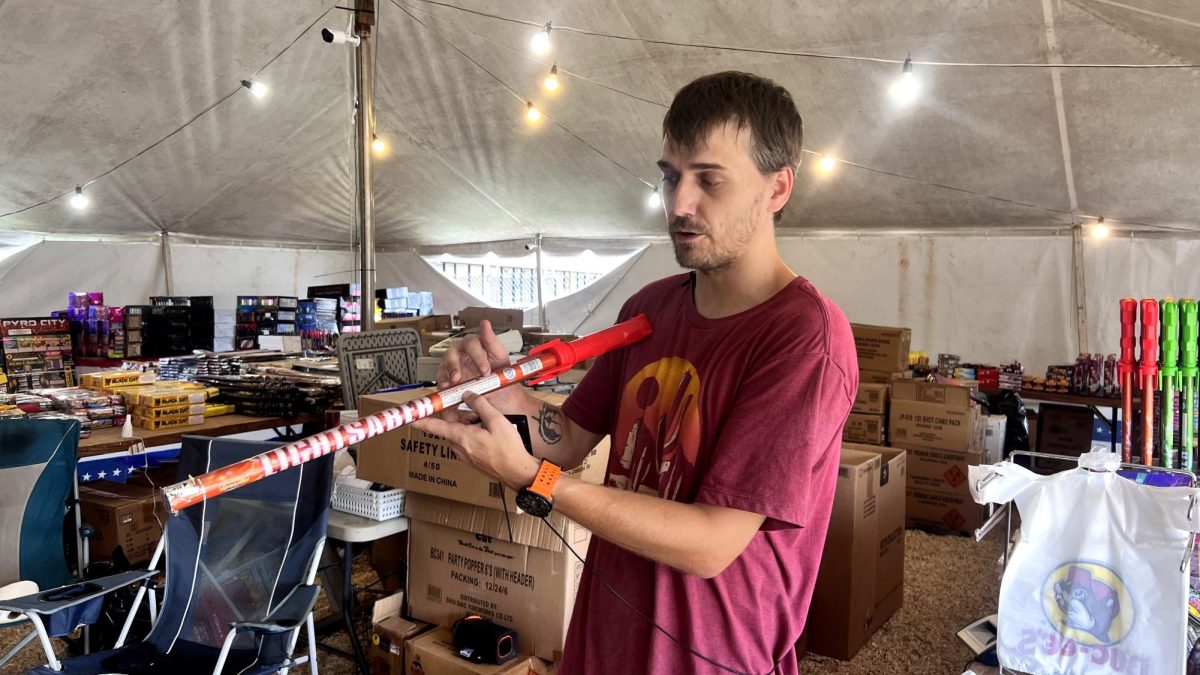 A man inside a fireworks tent points to the printed safety instructions on a large consumer firework.
