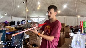 A man inside a fireworks tent points to the printed safety instructions on a large consumer firework.