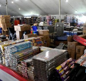 Tables inside a fireworks tent are stocked with consumer fireworks in boxes, tubes and assorted packages.