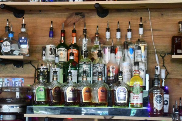 A range of liquor bottles sit on display behind a bar with a brown wooden wall behind it.