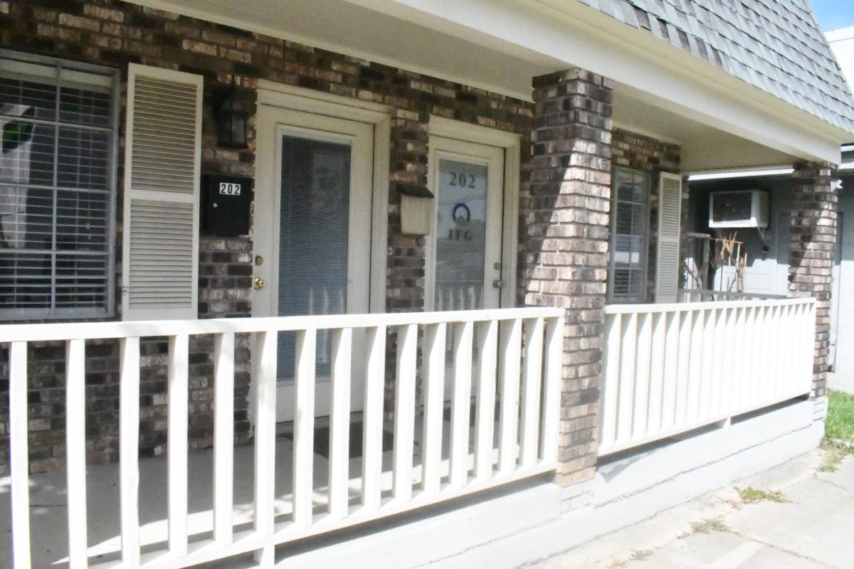 The exterior of a brick commercial building with a covered porch, white railing, and doors marked “202.”