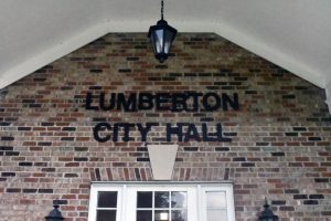 The words “Lumberton City Hall” are mounted on the brick exterior of the City Hall building.