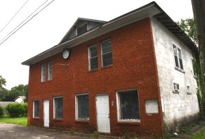 A two-story red brick building with a white-painted side wall and two white front doors.