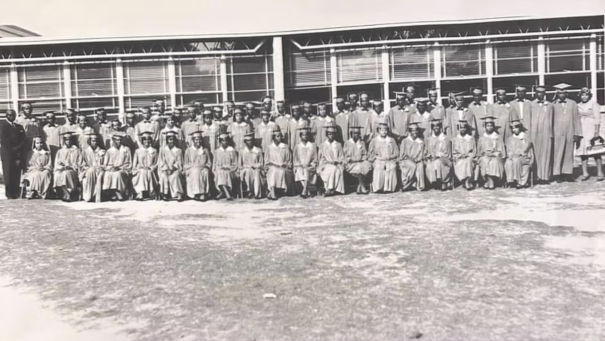 An undated black-and-white photo shows dozens of Magnolia High School graduates wearing caps and gowns while posing in front of the school building in Moss Point.