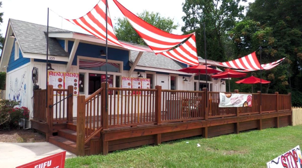 The exterior of Jamba Jollof restaurant with a wooden deck, striped awnings and outdoor seating.